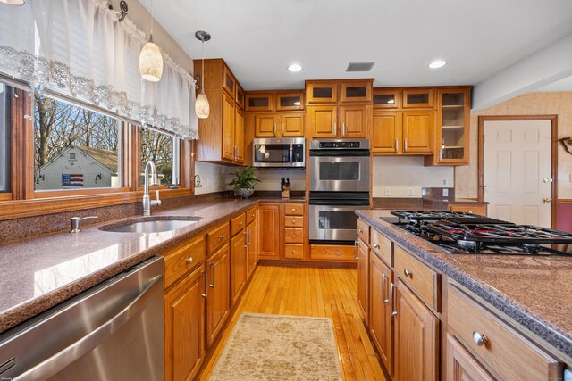 kitchen featuring sink, light hardwood / wood-style flooring, stainless steel appliances, decorative light fixtures, and dark stone counters