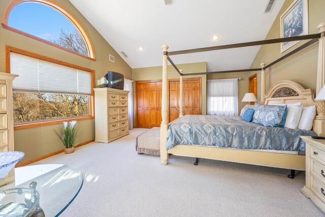 bedroom with light colored carpet, high vaulted ceiling, and two closets