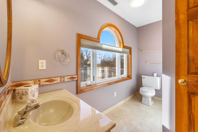 bathroom with toilet, vanity, visible vents, and baseboards