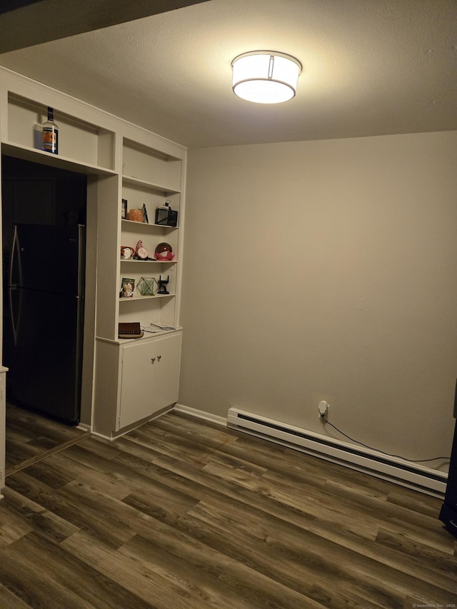 empty room with built in shelves, a baseboard radiator, and dark wood-type flooring