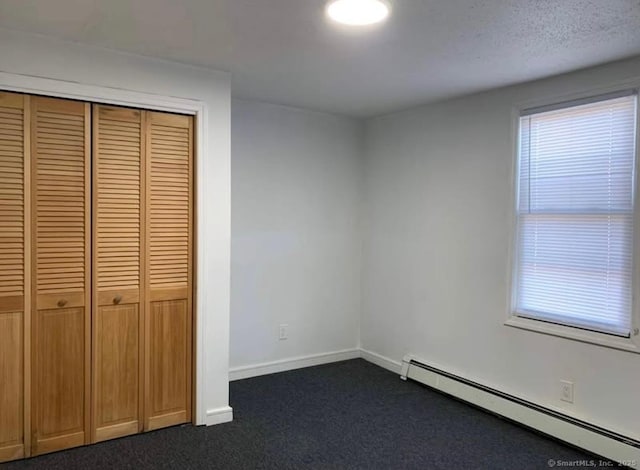 unfurnished bedroom with a baseboard radiator, dark carpet, a closet, and multiple windows