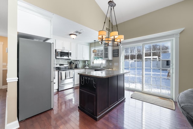 kitchen featuring a center island, hanging light fixtures, appliances with stainless steel finishes, dark stone counters, and white cabinets