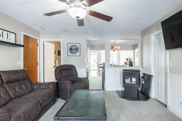 living room featuring ceiling fan with notable chandelier, a wood stove, and light colored carpet