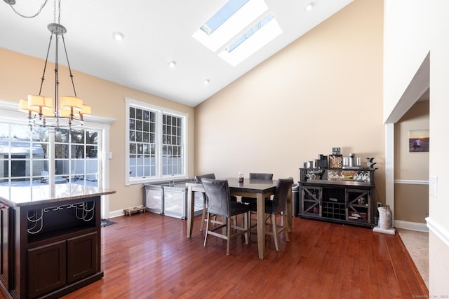 dining area with dark wood-type flooring, a skylight, high vaulted ceiling, and a notable chandelier