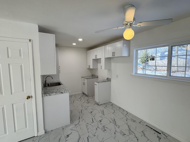 kitchen with white cabinetry, light stone countertops, sink, and ceiling fan