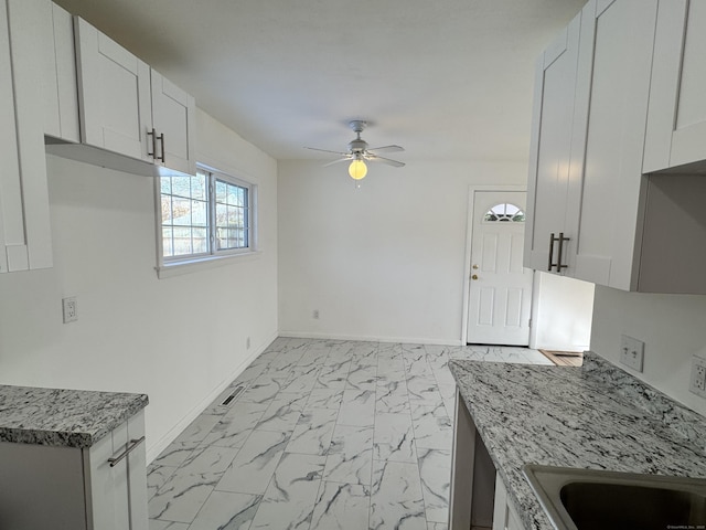 kitchen featuring ceiling fan, white cabinets, and light stone counters