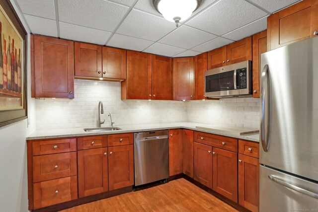 kitchen with sink, light stone counters, light wood-type flooring, appliances with stainless steel finishes, and backsplash