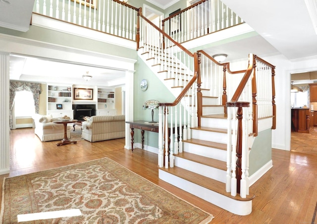 stairway featuring crown molding, wood-type flooring, built in shelves, and a high ceiling