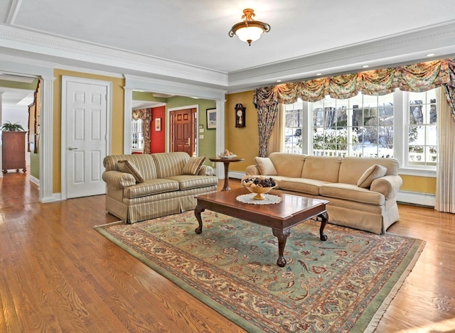 living room with a baseboard heating unit, crown molding, decorative columns, and light wood-type flooring