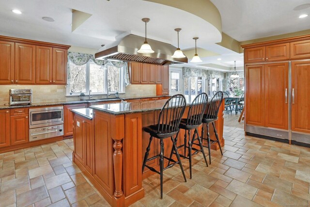 kitchen with a kitchen island, stainless steel microwave, dark stone countertops, a kitchen bar, and hanging light fixtures