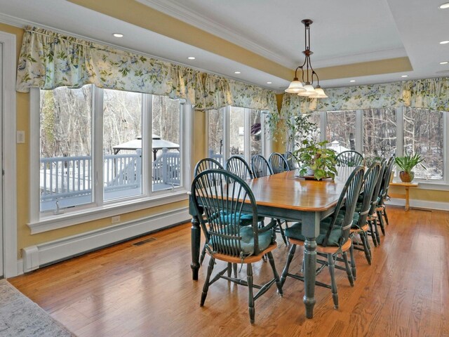 dining space featuring a raised ceiling, ornamental molding, baseboard heating, and light hardwood / wood-style floors