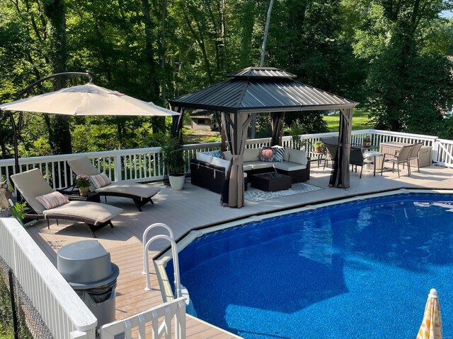 view of pool featuring a wooden deck, a gazebo, and an outdoor living space with a fire pit