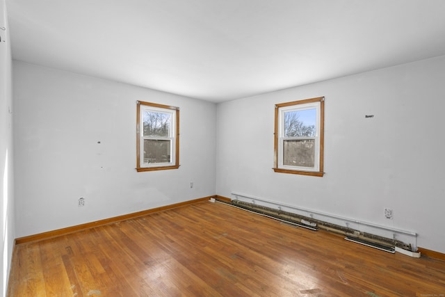 unfurnished room featuring hardwood / wood-style flooring, plenty of natural light, and a baseboard heating unit