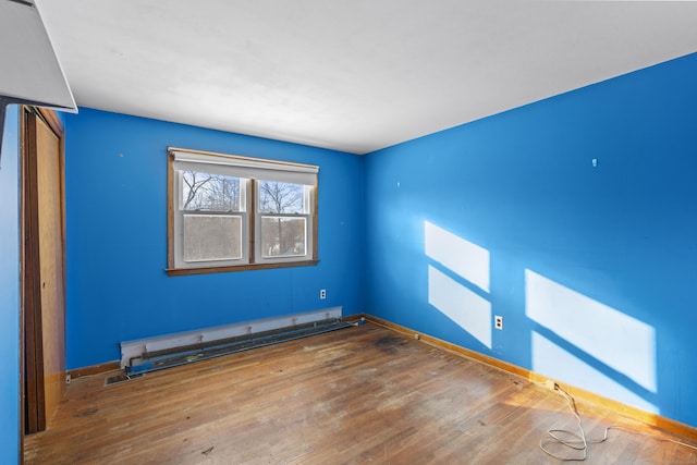 unfurnished room featuring hardwood / wood-style floors and a baseboard heating unit