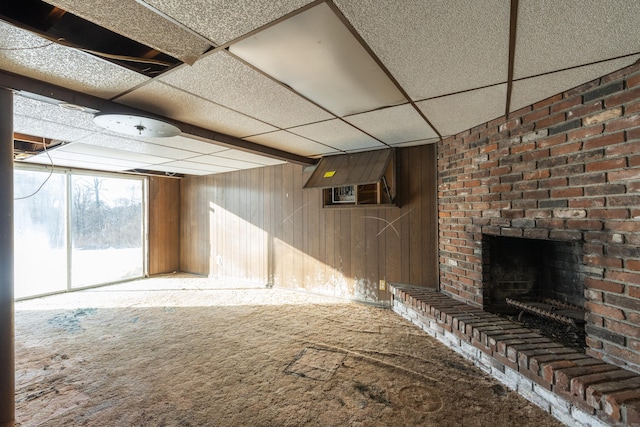 basement with a fireplace, wooden walls, carpet, and a drop ceiling