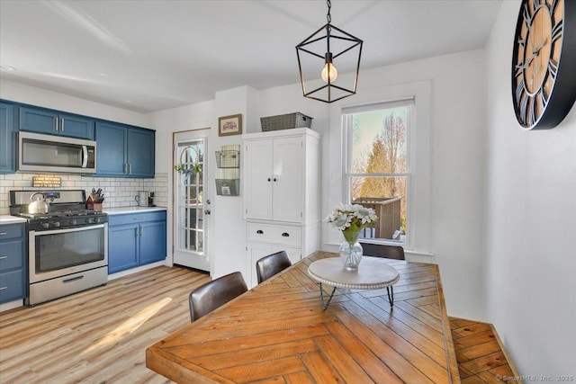 kitchen featuring blue cabinets, tasteful backsplash, light hardwood / wood-style flooring, appliances with stainless steel finishes, and pendant lighting