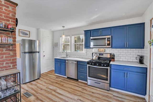 kitchen with blue cabinets, tasteful backsplash, light hardwood / wood-style flooring, appliances with stainless steel finishes, and pendant lighting