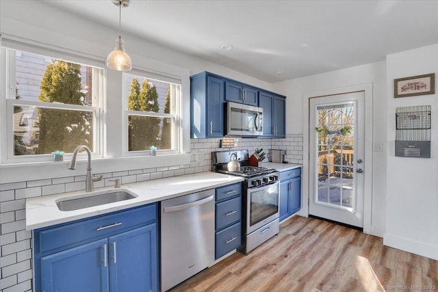 kitchen with blue cabinetry, sink, tasteful backsplash, decorative light fixtures, and stainless steel appliances