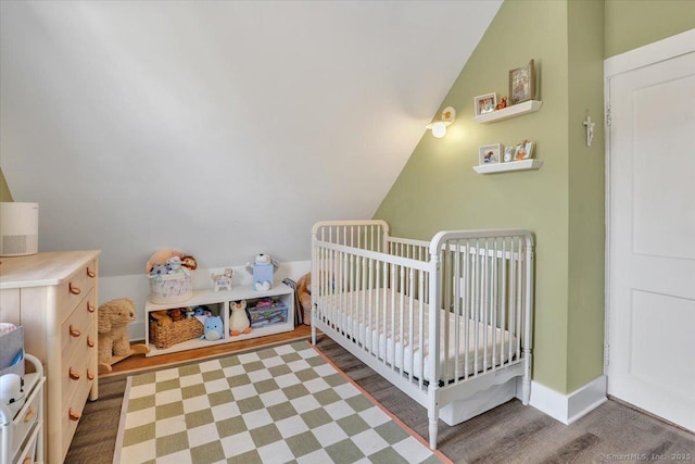 bedroom with dark hardwood / wood-style flooring, a crib, and vaulted ceiling