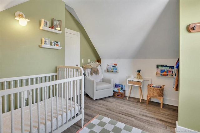 bedroom featuring lofted ceiling, wood-type flooring, and a crib