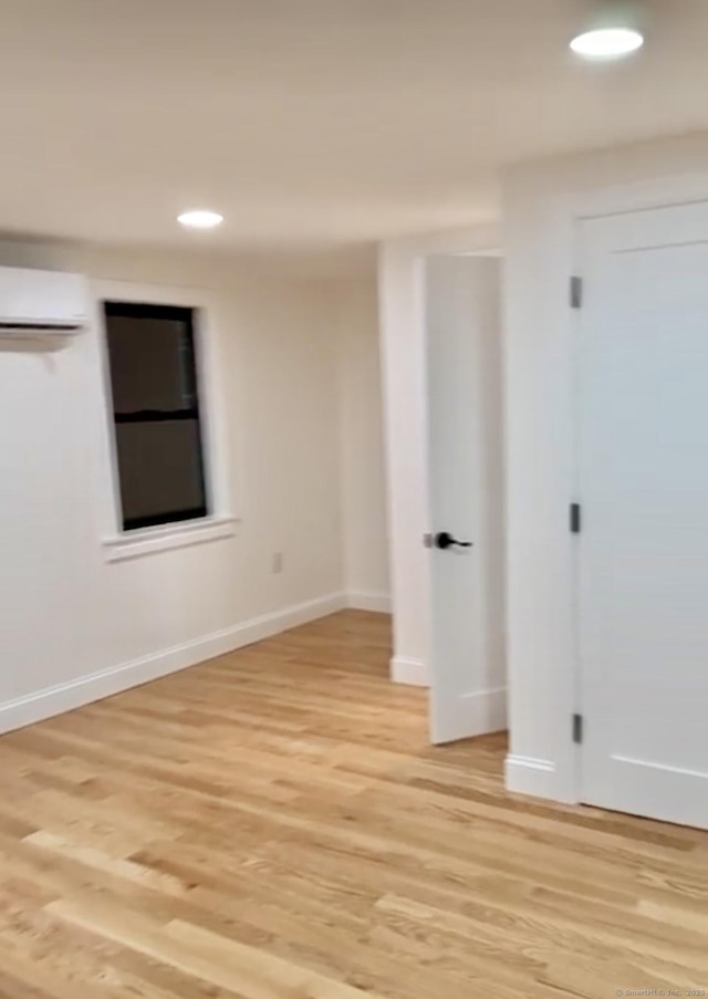 empty room featuring a wall mounted AC and light hardwood / wood-style flooring