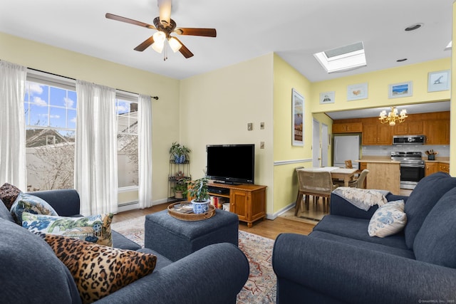 living room with baseboard heating, a skylight, ceiling fan with notable chandelier, and light wood-type flooring