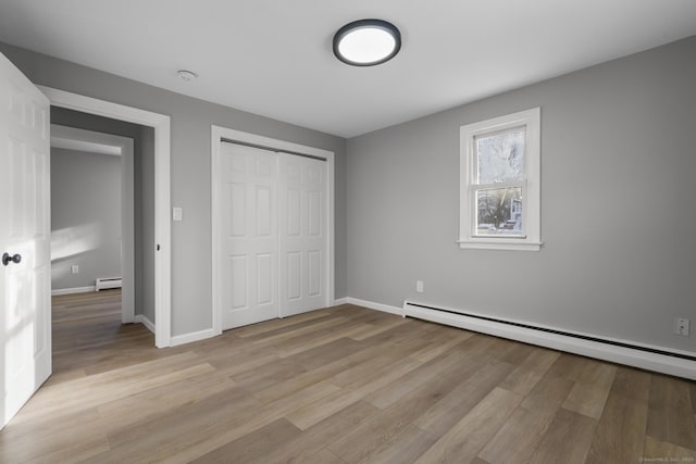 unfurnished bedroom with a baseboard radiator, a closet, and light hardwood / wood-style flooring