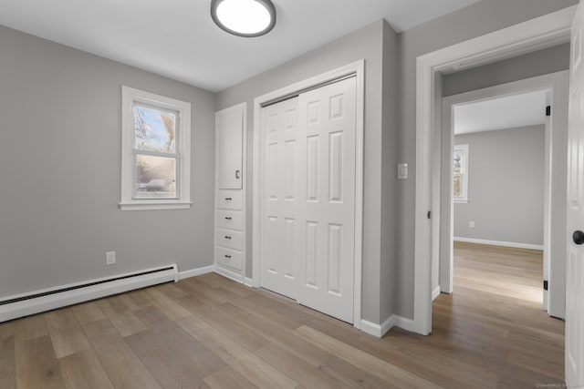 unfurnished bedroom with light hardwood / wood-style floors, a closet, and baseboard heating