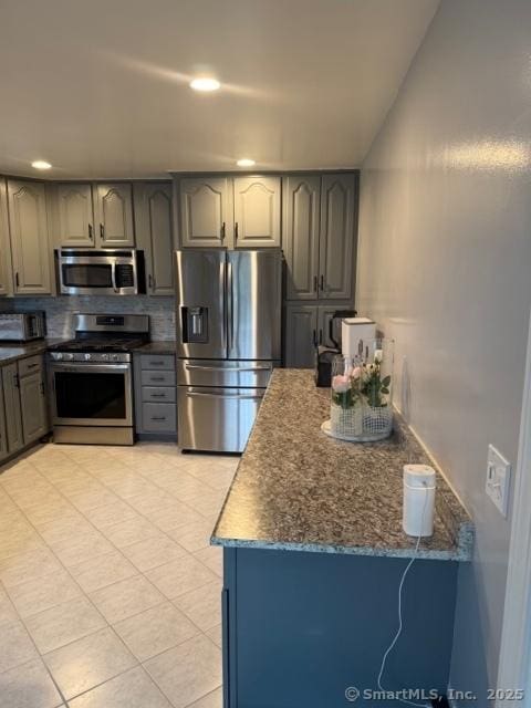 kitchen with dark stone countertops, light tile patterned floors, tasteful backsplash, and stainless steel appliances