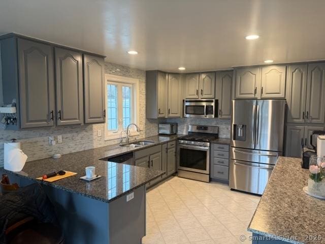 kitchen featuring sink, dark stone counters, kitchen peninsula, stainless steel appliances, and decorative backsplash