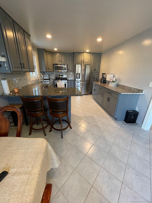 kitchen featuring appliances with stainless steel finishes, gray cabinetry, tasteful backsplash, a kitchen bar, and kitchen peninsula