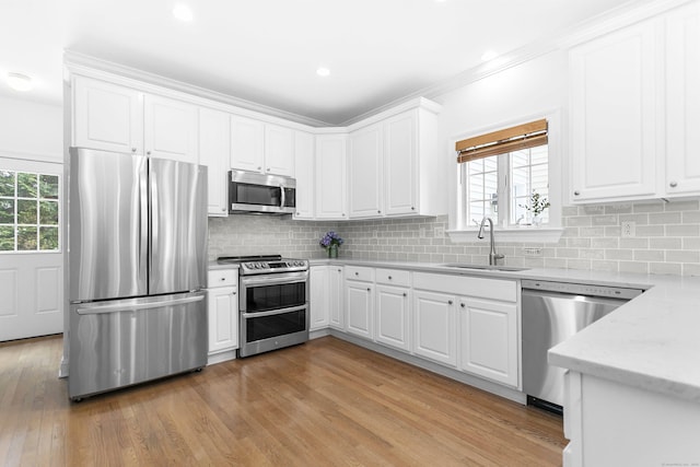 kitchen with light hardwood / wood-style flooring, stainless steel appliances, decorative backsplash, sink, and white cabinetry