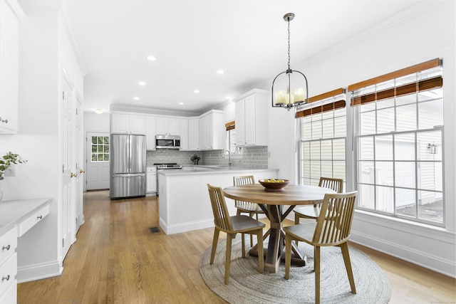 dining space featuring a notable chandelier, light hardwood / wood-style floors, sink, and ornamental molding