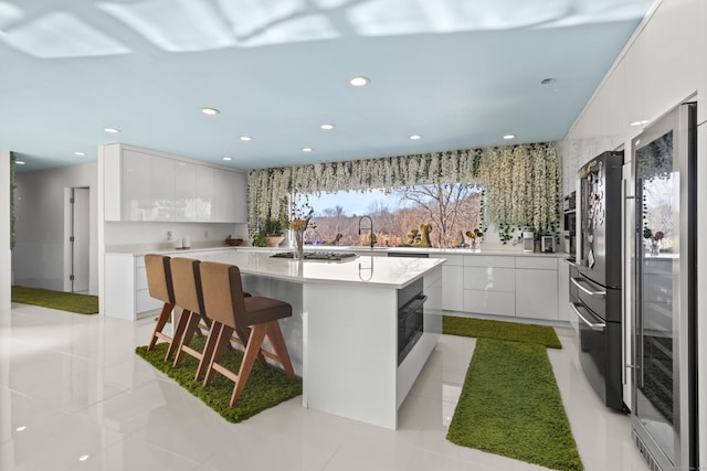 kitchen featuring a kitchen bar, sink, light tile patterned floors, a kitchen island with sink, and white cabinets