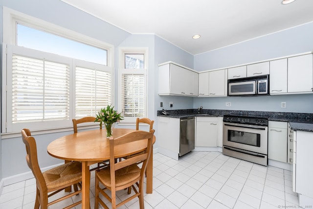 kitchen with white cabinetry, appliances with stainless steel finishes, light tile patterned floors, and dark stone countertops