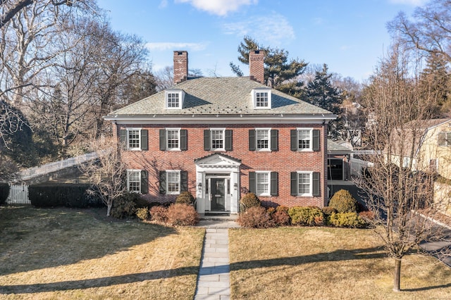 georgian-style home with brick siding, a chimney, a front yard, and fence