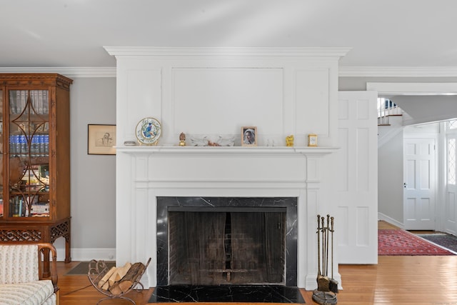 interior details featuring baseboards, a premium fireplace, ornamental molding, and wood finished floors