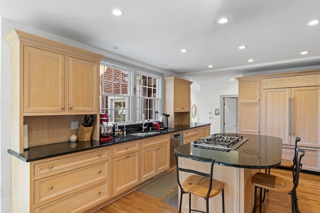 kitchen featuring stainless steel appliances, a sink, light wood-type flooring, light brown cabinetry, and a kitchen bar