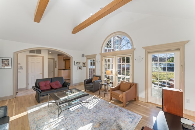 living room featuring baseboards, arched walkways, beamed ceiling, light wood-style floors, and high vaulted ceiling