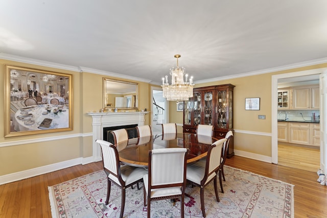 dining room with a fireplace, baseboards, ornamental molding, light wood finished floors, and an inviting chandelier