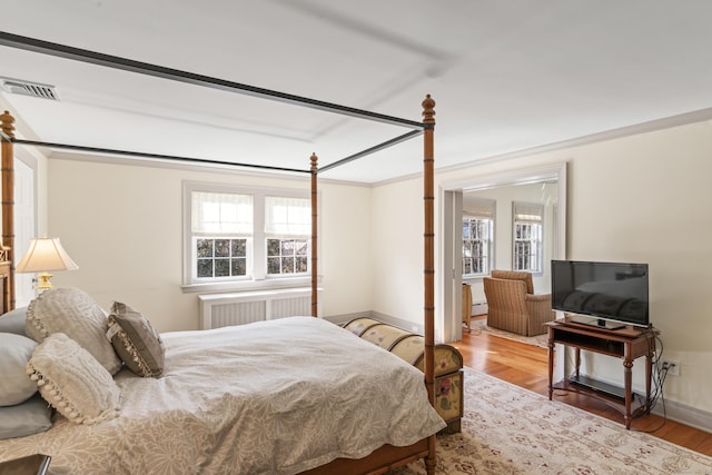 bedroom with multiple windows, visible vents, radiator heating unit, and wood finished floors