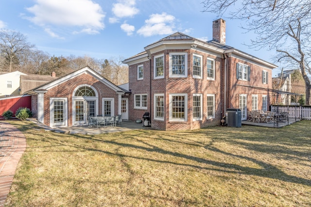 back of house featuring brick siding, a chimney, central air condition unit, a lawn, and a patio area