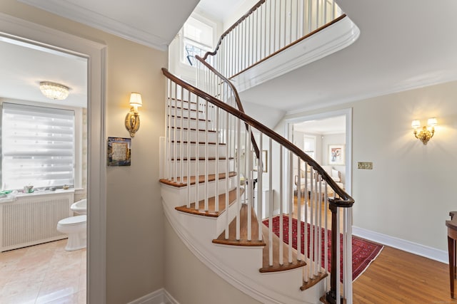 stairs featuring radiator heating unit, baseboards, crown molding, and wood finished floors