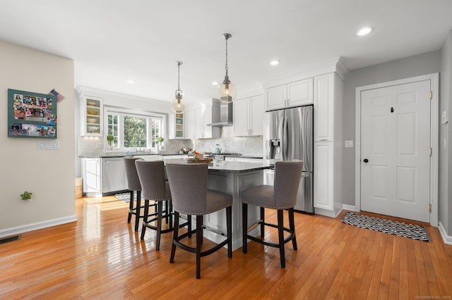 kitchen with wall chimney exhaust hood, appliances with stainless steel finishes, a kitchen island, light stone countertops, and white cabinets