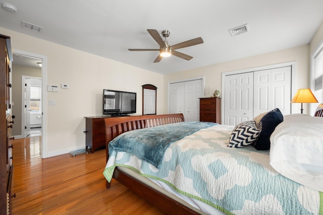 bedroom featuring hardwood / wood-style flooring, ceiling fan, and multiple closets