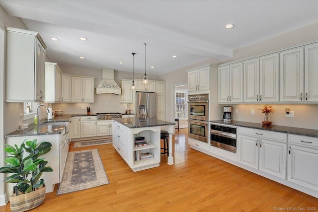 kitchen with sink, custom exhaust hood, appliances with stainless steel finishes, a kitchen island, and white cabinets