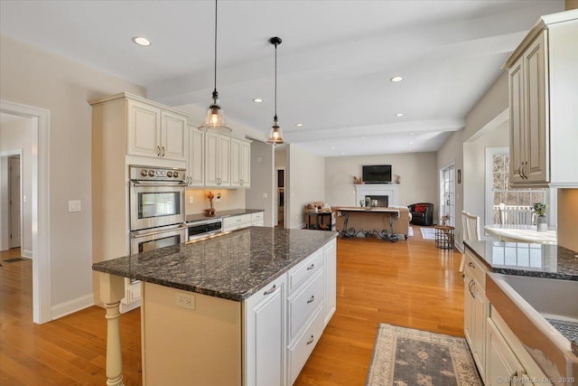 kitchen featuring light hardwood / wood-style flooring, a kitchen island, pendant lighting, stainless steel double oven, and cream cabinetry