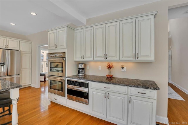 kitchen with beamed ceiling, white cabinetry, appliances with stainless steel finishes, and light wood-type flooring