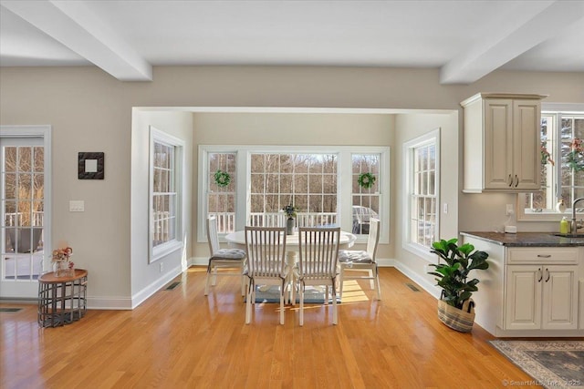 dining room with beamed ceiling, plenty of natural light, and light hardwood / wood-style floors