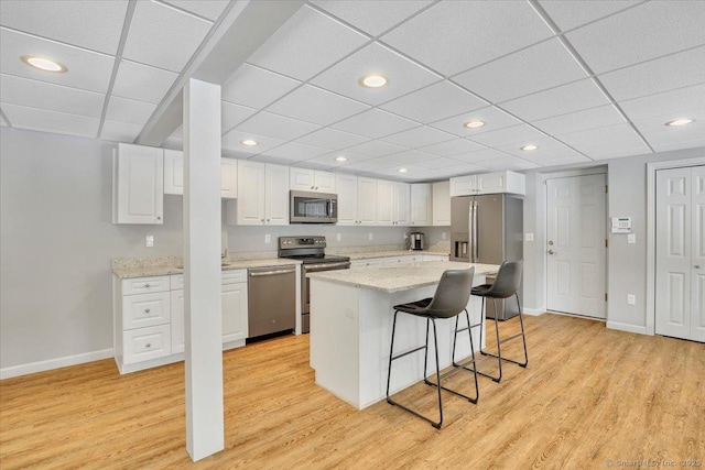 kitchen with a breakfast bar, appliances with stainless steel finishes, a center island, white cabinets, and light wood-type flooring